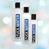 Displayed against a soft-focus, multicolored background are three bottles of "Fuck Water Original" lubricant, featuring a sleek white base with bold black labels and blue text.